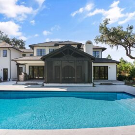 A rectangular pool with curved edge sits in front of a new home, with a screened in room overlooking the pool. The pool's waterline is decorated with blue patterned tiles. Shallow steps reach across the width of the pool on the right-hand side. Golden Seas Outdoors finished the pool in Diamond Brite Classic exposed aggregate pool finish.